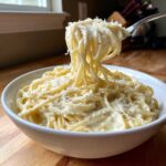 A fork lifts creamy pasta coated in rich homemade alfredo sauce, topped with grated Parmesan cheese.