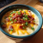 Close-up of a creamy potato soup recipe topped with shredded cheddar cheese, bacon bits, and chopped green onions.