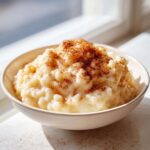 A creamy bowl of old-fashioned rice pudding topped generously with ground cinnamon, bathed in natural light.