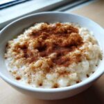 A close-up of creamy rice pudding recipe served in a white bowl, generously dusted with cinnamon.