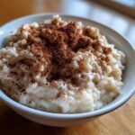 A close-up of a creamy bowl of rice pudding recipe generously dusted with ground cinnamon.