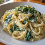 A close-up, appetizing shot of creamy spinach pasta tossed in a rich white sauce, garnished with fresh parsley.