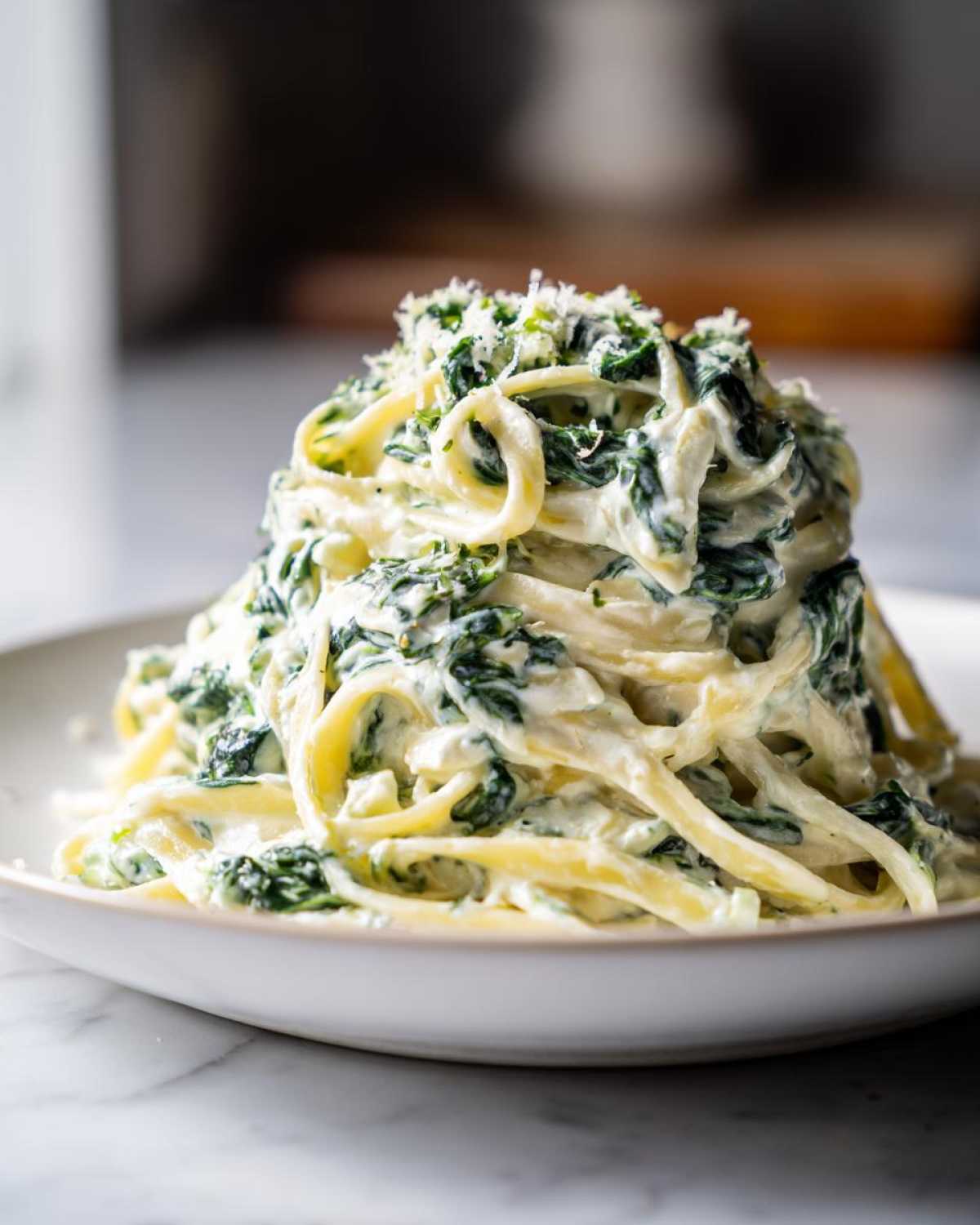 A close-up of creamy spinach pasta tossed in a rich white sauce and topped with grated Parmesan cheese.