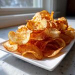 A large pile of golden brown, crispy air fryer potato chips served on a white rectangular plate.
