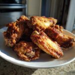 A close-up of perfectly crispy, golden brown fried chicken wings piled high on a white plate.