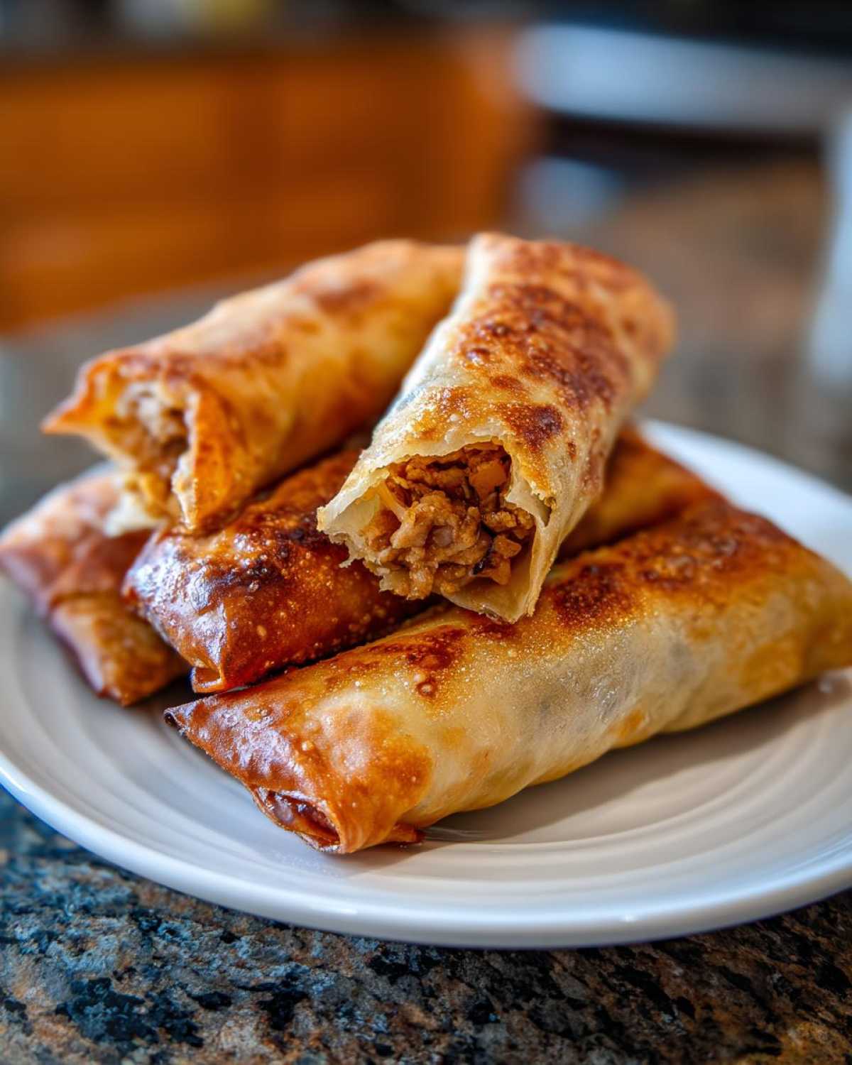 Close-up of several crispy, golden-brown homemade egg roll appetizers stacked on a white plate.