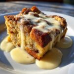 A close-up of a warm slice of bread pudding generously topped with creamy vanilla sauce.