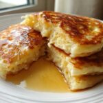 Close-up of fluffy buttermilk pancakes stacked and broken open, drizzled with golden syrup.