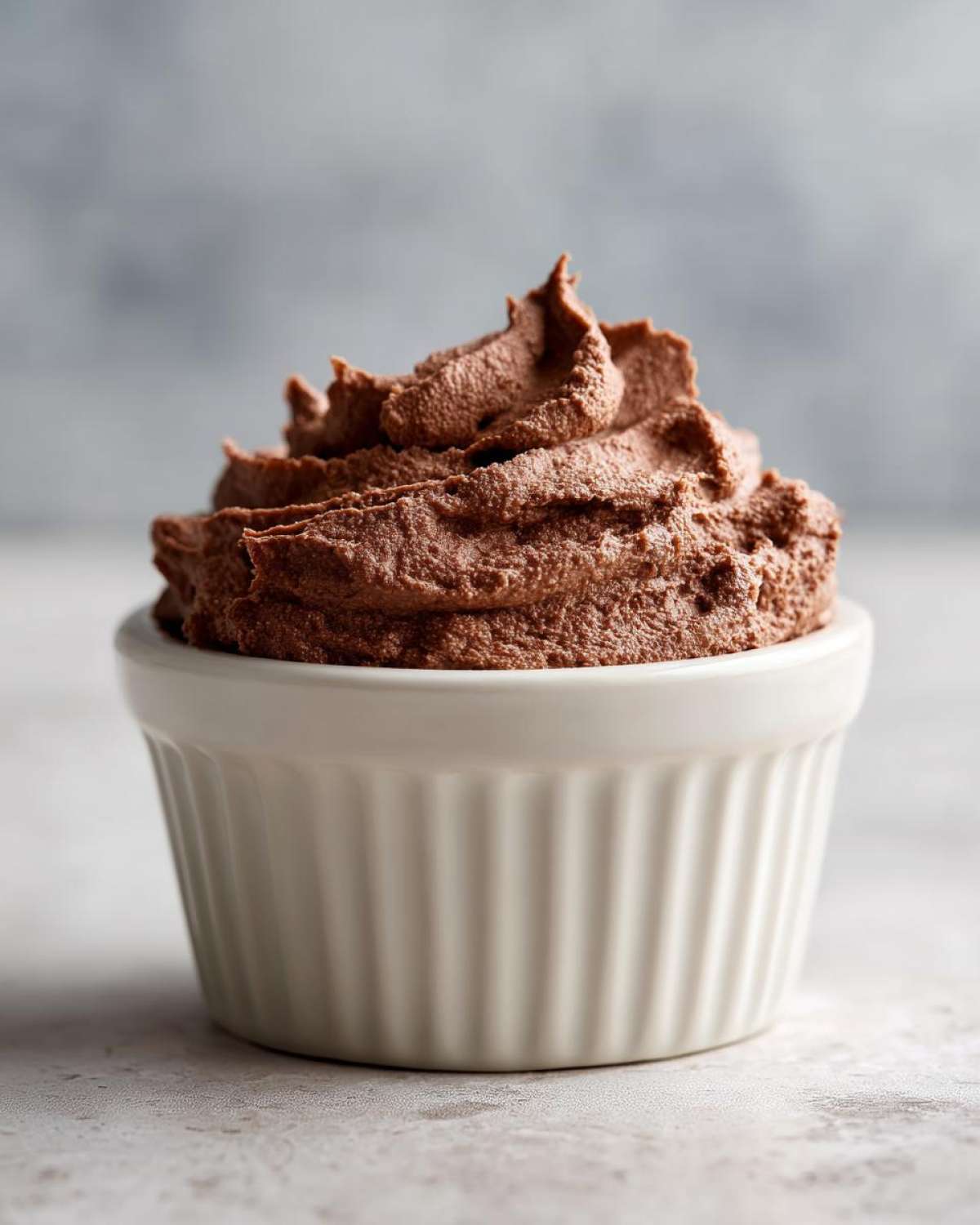 A close-up of rich, dark chocolate mousse piped high in a white, fluted ramekin.