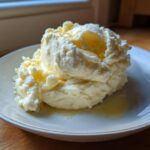 A scoop of creamy, fluffy slow cooker mashed potatoes topped with melted butter on a light-colored plate.