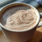 Close-up of a mug filled with frothy white hot chocolate, showing a swirl pattern on top.
