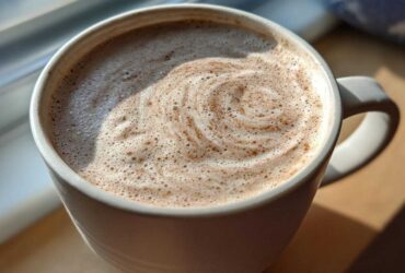 Close-up of a mug filled with frothy white hot chocolate, showing a swirl pattern on top.