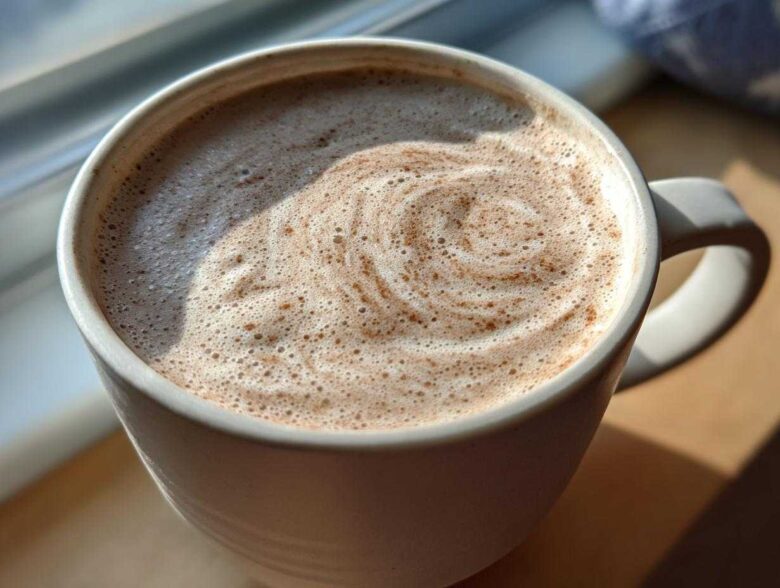 Close-up of a mug filled with frothy white hot chocolate, showing a swirl pattern on top.
