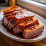 Close-up of thick, glazed slices of candied yams resting in a rich, dark syrup on a white platter.