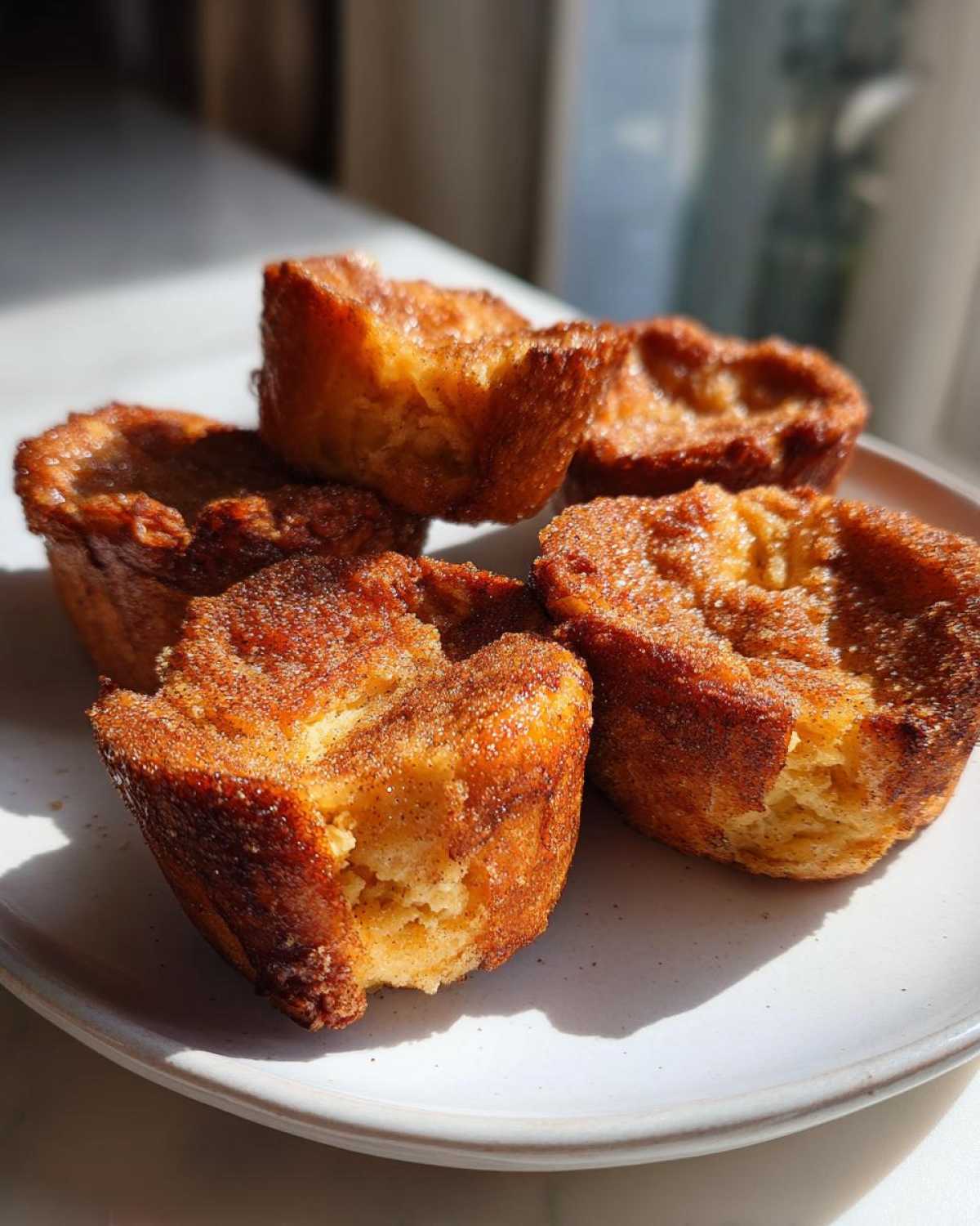 Four golden brown french toast muffins dusted with cinnamon sugar sitting on a light plate.