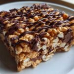 A close-up of a gooey peanut butter rice krispie treats square drizzled with melted chocolate.
