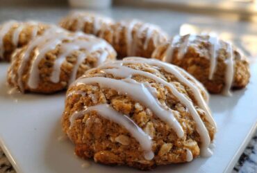 Close-up of soft, gooey persimmon cookies drizzled with white vanilla glaze on a white platter.