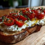 A slice of toasted bread topped with creamy ricotta, roasted cherry tomatoes, olive oil, and fresh thyme for a perfect ricotta toast.