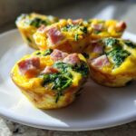 Close-up of several savory ham and spinach egg muffin cups served on a white plate.