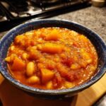 Close-up of a rich, orange butternut squash chili with white beans served in a dark blue ceramic bowl.