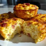 A close-up shot showing several golden-brown, high-protein egg bites, with one cut open to reveal a fluffy interior with bacon pieces.