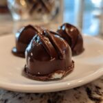 Close-up of three homemade chocolate covered cherries resting on a white plate, showing the glossy dark chocolate coating.