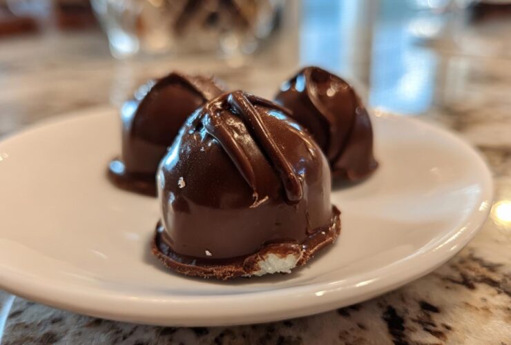 Close-up of three homemade chocolate covered cherries resting on a white plate, showing the glossy dark chocolate coating.