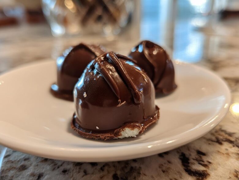 Close-up of three homemade chocolate covered cherries resting on a white plate, showing the glossy dark chocolate coating.