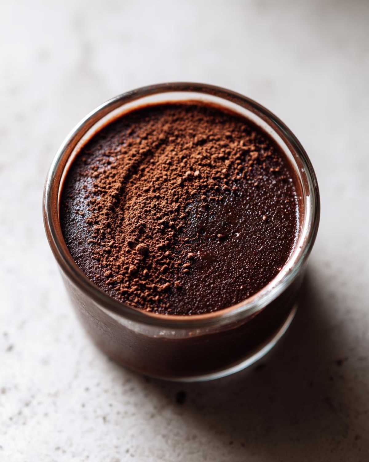 Overhead view of rich homemade chocolate pudding topped with a dusting of cocoa powder in a small glass.