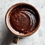 Overhead close-up of thick, rich homemade chocolate pudding swirled inside a dark brown, rustic ceramic mug.