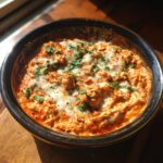 Close-up of hot chicken enchilada dip topped with melted white cheese and fresh cilantro.