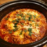 Close-up of bubbling chicken enchilada dip topped with melted cheese and fresh cilantro in a black slow cooker.