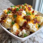 Close-up of loaded baked potato salad topped with melted cheddar cheese, bacon bits, and green onions.