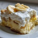 Close-up of a single serving of creamy banana pudding layered with vanilla wafers and topped with whipped cream and banana slices.