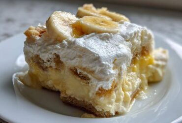 Close-up of a single serving of creamy banana pudding layered with vanilla wafers and topped with whipped cream and banana slices.