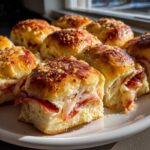 Close-up of freshly baked pizza sliders oozing melted cheese and pepperoni on a white plate.