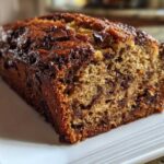 Close-up of a slice of moist banana bread recipe, featuring a dark, caramelized crust and visible chocolate chips.