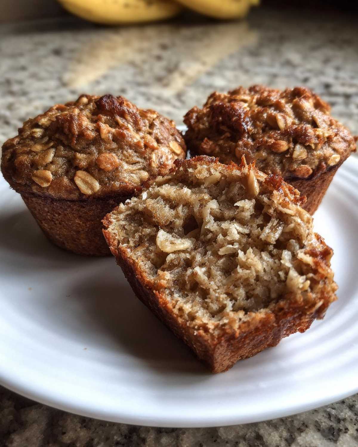 Close-up of banana oatmeal muffins, one split open showing the moist, textured interior with visible oats.