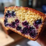 Close-up of a moist slice of blueberry banana bread showing a golden crumb and dense, juicy blueberries.