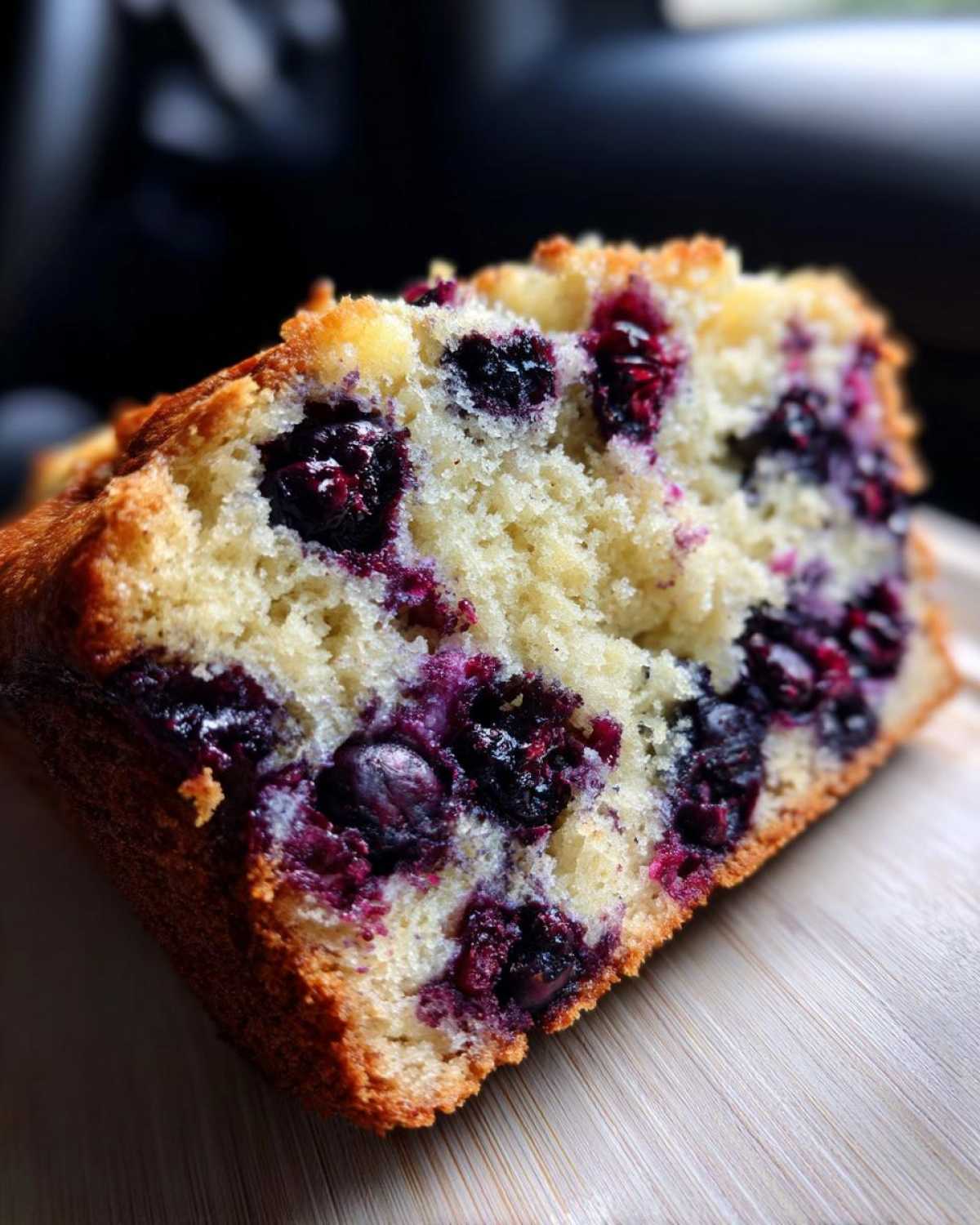 Close-up of a moist slice of blueberry banana bread showing bright purple blueberries baked into the crumb.
