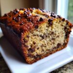 A close-up of a moist chocolate chip banana bread recipe loaf, showing the rich brown crust and soft interior.