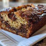 A close-up of a moist slice of chocolate chip banana bread recipe loaf with melted chocolate drizzled on top.
