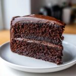 Close-up of a thick slice of moist homemade chocolate cake layered with dark chocolate frosting.