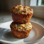 Two golden-brown oatmeal muffins stacked on a white plate, showcasing a moist, textured top.