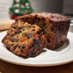 Close-up of a moist traditional fruit cake, showing rich dark dried fruit and candied peel inside, served on a white plate.
