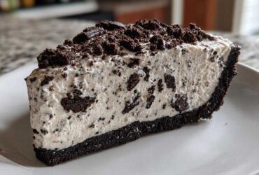 A thick slice of creamy no-bake oreo pie with a dark chocolate crust and topped with crushed oreos.