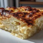 A close-up of a rich, creamy slice of potatoes au gratin showing layered potatoes and a deeply browned, cheesy crust.