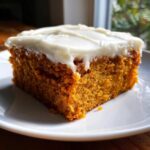Close-up of a moist, orange pumpkin bar topped with thick, white cream cheese frosting.