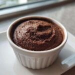 A close-up of rich, dark chocolate mousse served in a white, fluted ramekin.