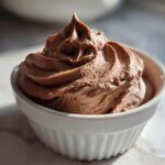 A close-up of rich, airy chocolate mousse piped high in a white ramekin dish.